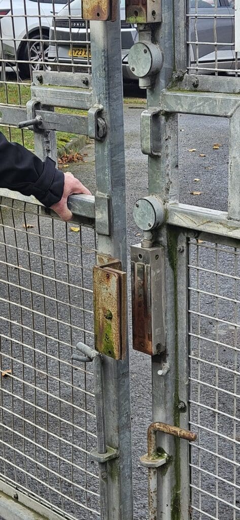 Security consultant inspecting a defective magnetic lock on an industrial site access gate.